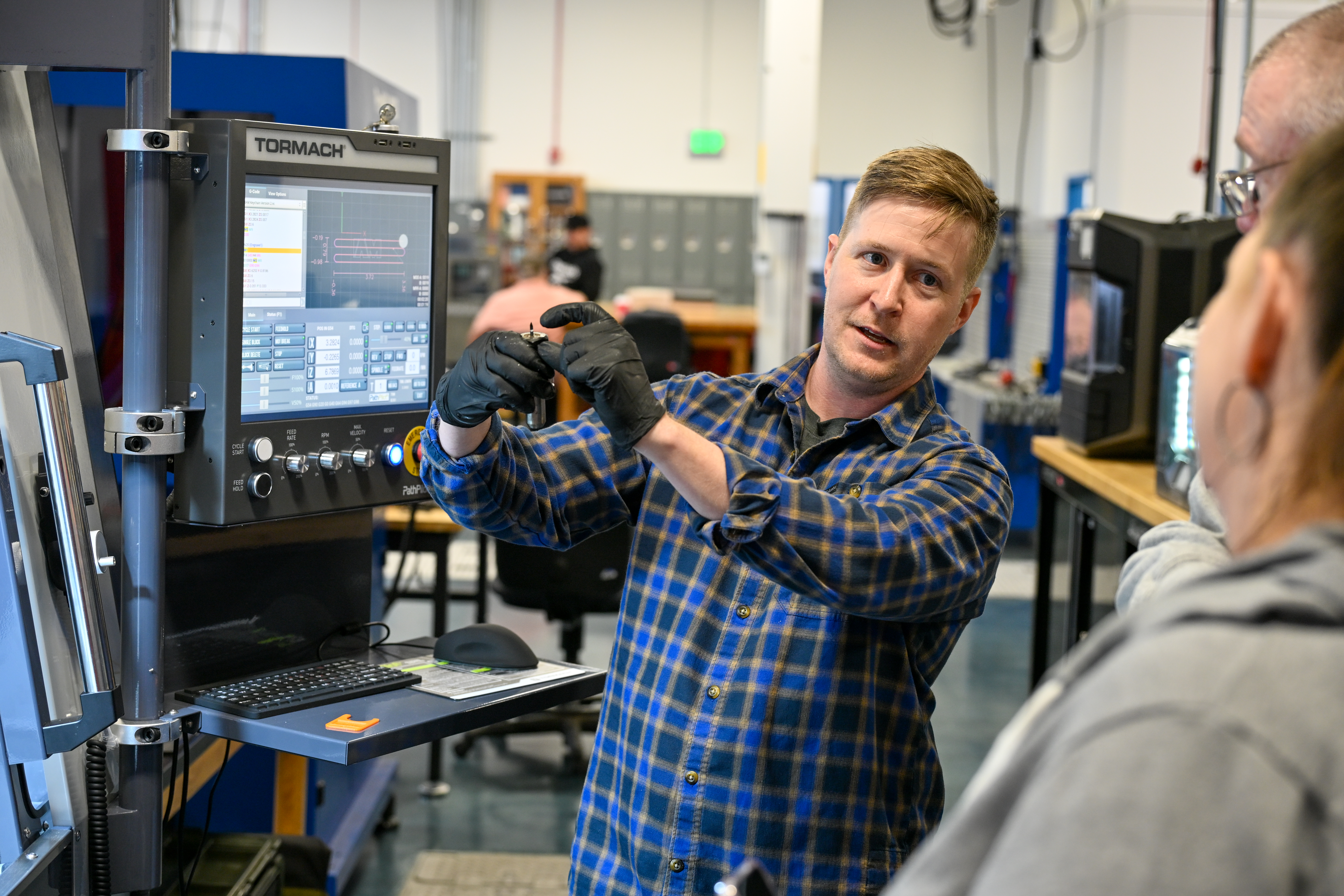 Instructor speaking to a man and woman next to machinery