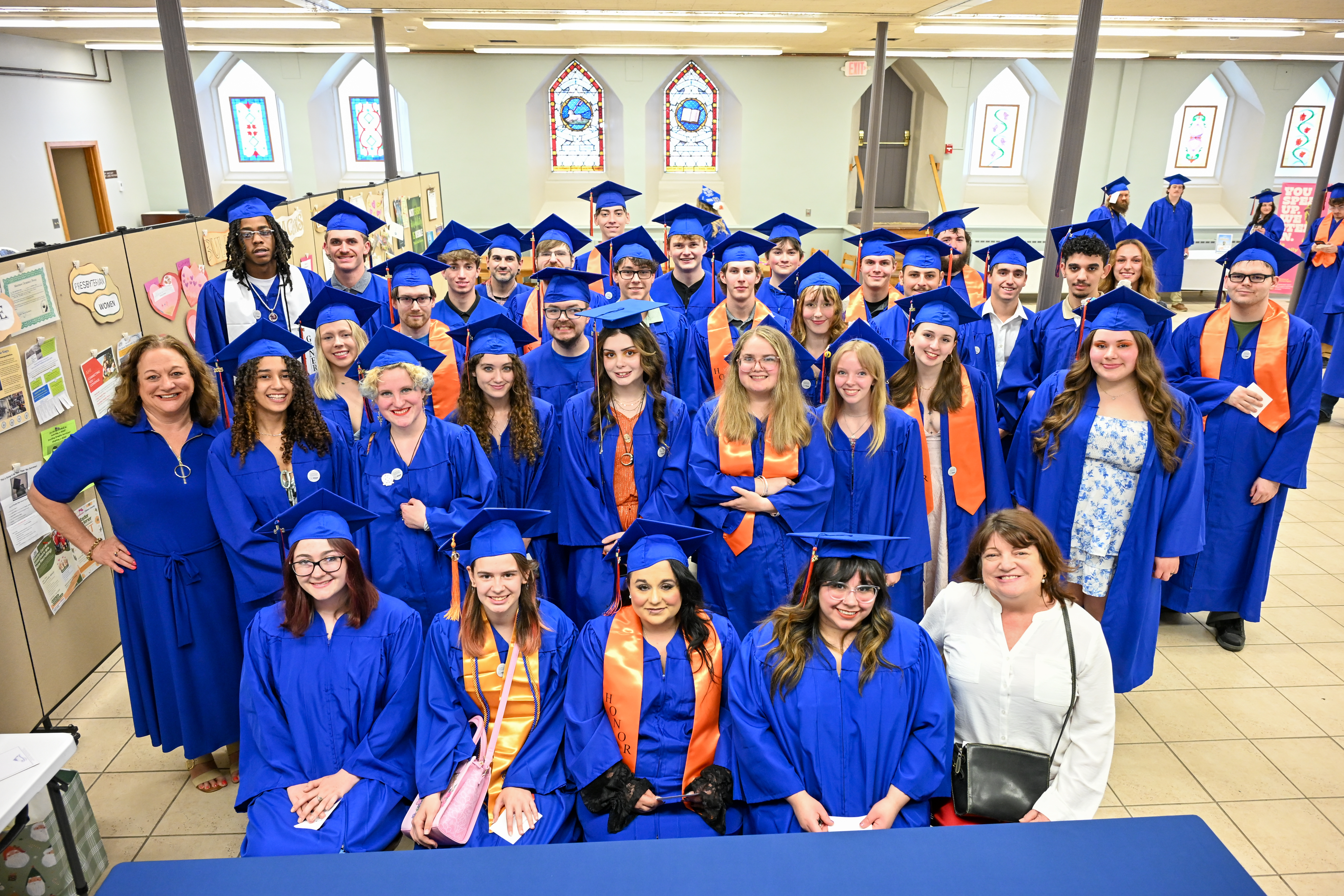 Dozens of students wearing graduation regalia in a church setting