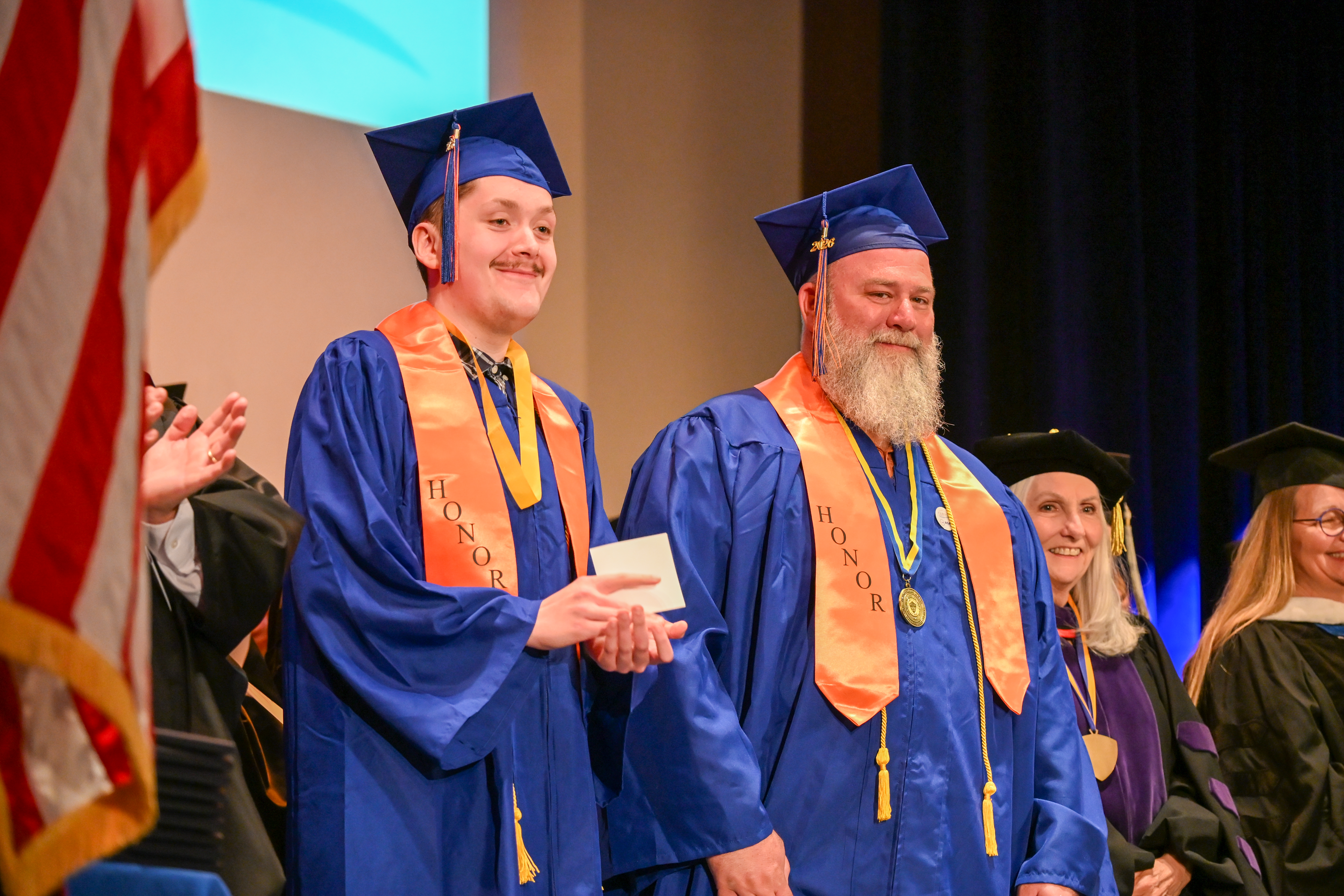 Two students wearing graduation regalia including stoles that have 'honor' embroidered