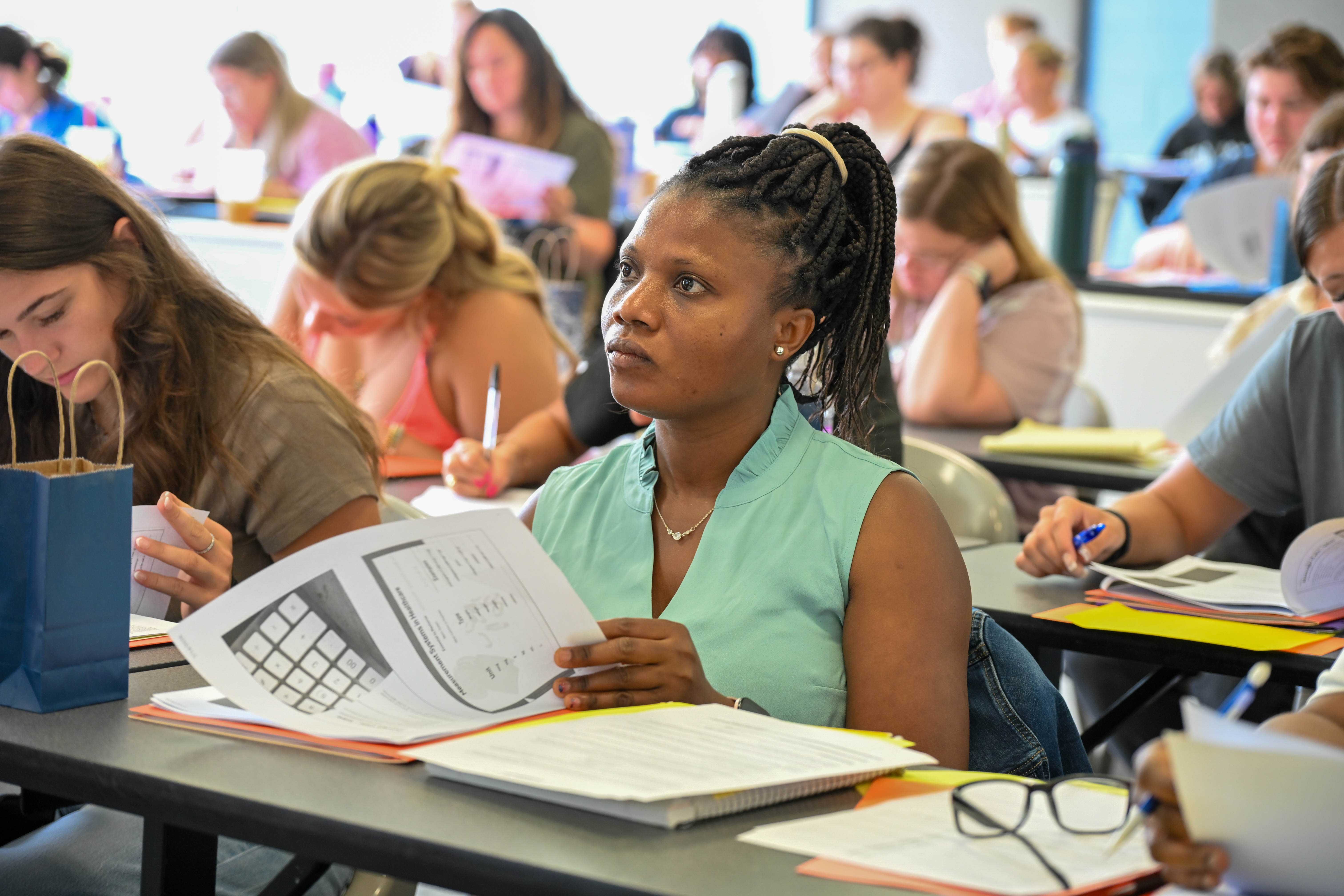 A student paying attention in class flipping through papers with other students in the background