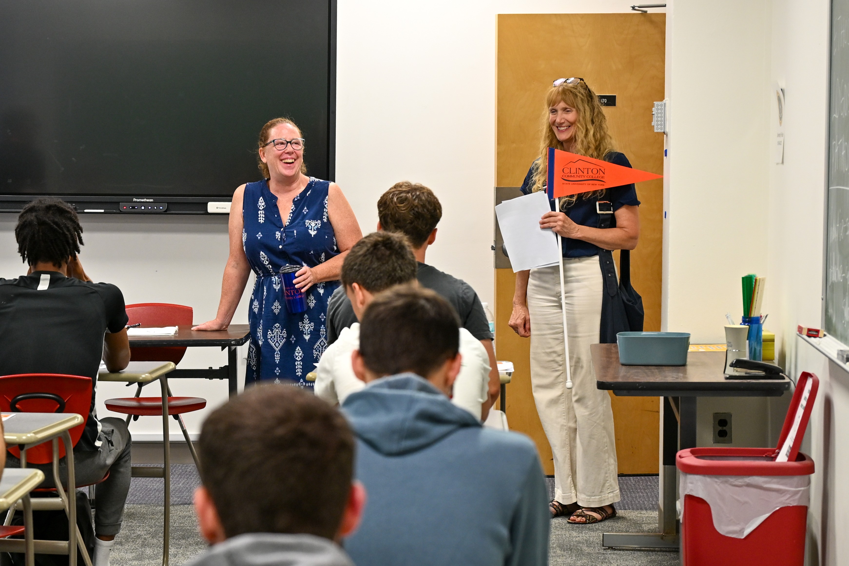 Two instructors stand at the front of a classroom with students sitting before them