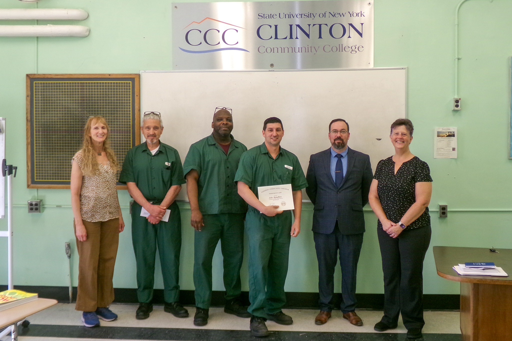 Six people standing together with three students in the center, one holding a certificate